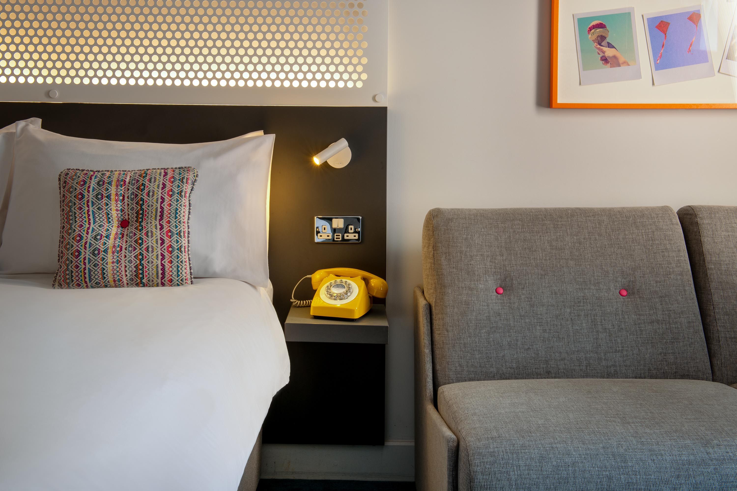 Close up with bed and sofa with yellow phone on bedside table
